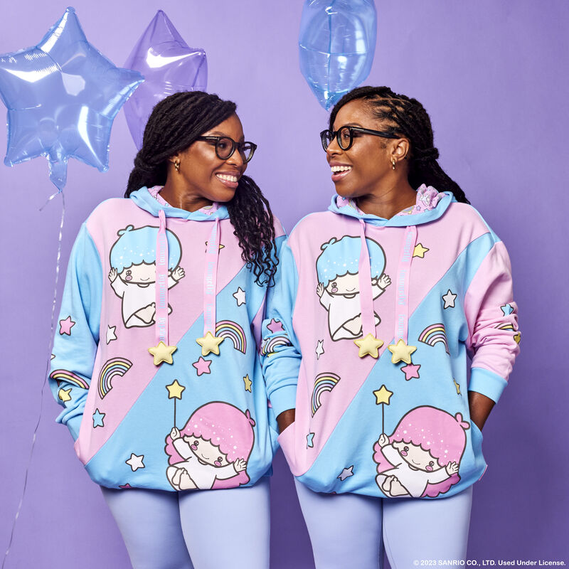 Set of female twins both wearing the blue and pink Little Twin Stars Unisex Hoodie against a purple background with blue and purple balloons